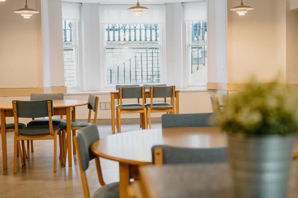 A dining area with tables and chairs, large windows with a view of a staircase, and pendant lighting.