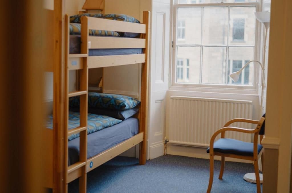 A bunk bed with a window and a chair in a room with a radiator.