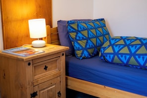 A wooden bedside table with a lamp, a bed with blue bedding, and patterned pillows.