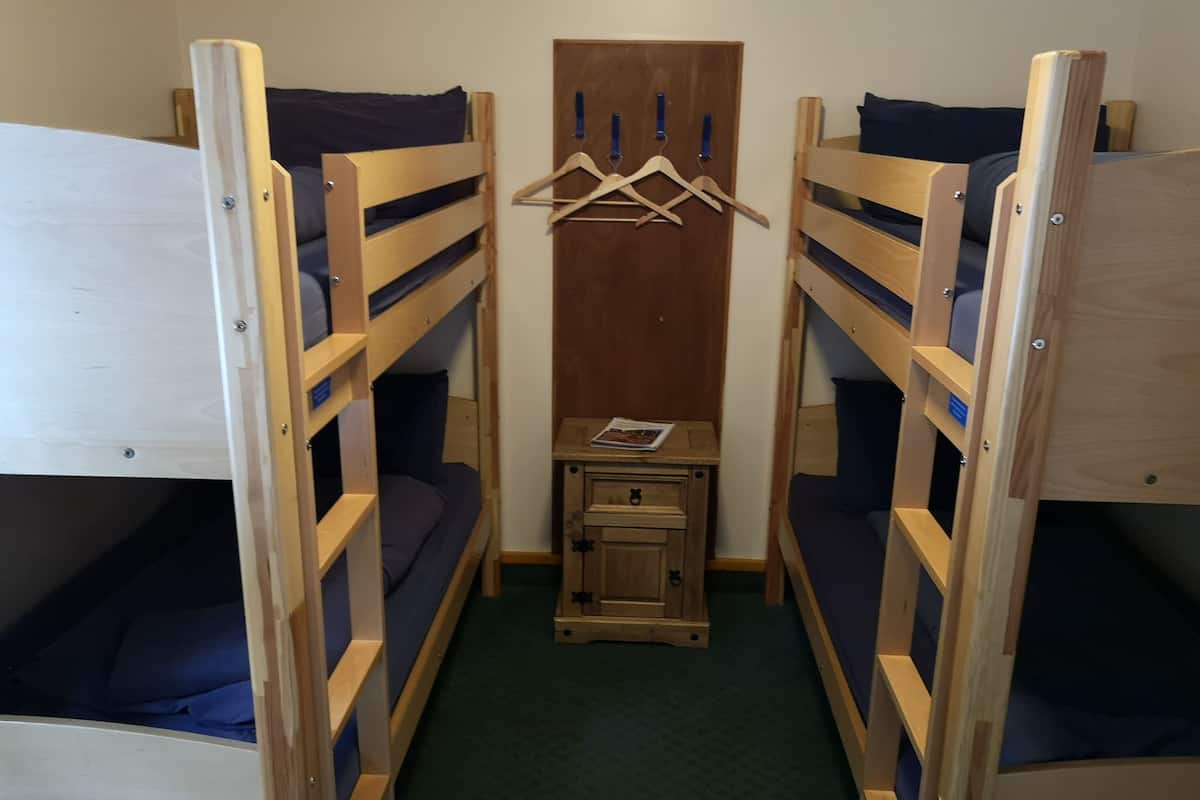 A compact room with two bunk beds, a small wooden cabinet, and a wooden hanger rack.