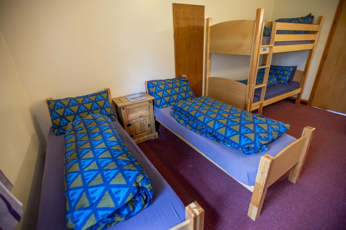 A dormitory room with two single beds, a wooden nightstand, and a bunk bed.