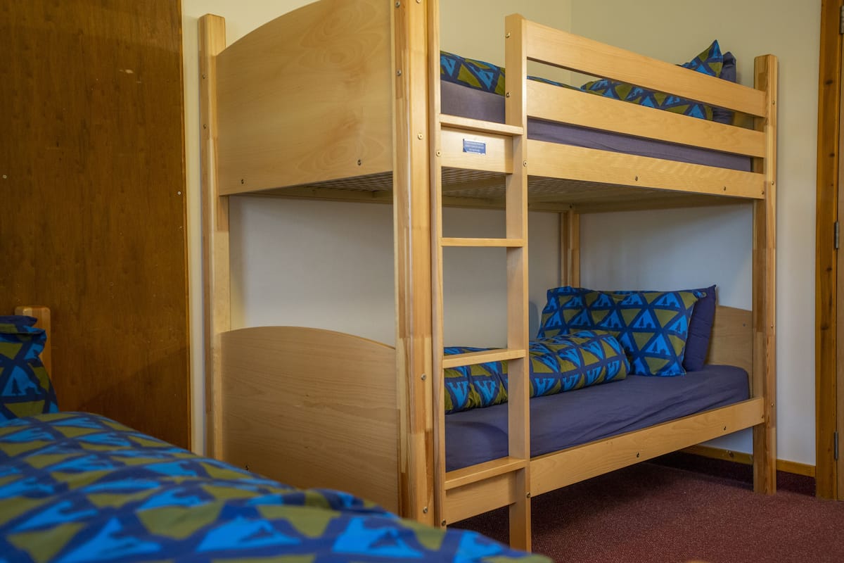 A bunk bed with a ladder, a wooden headboard, and a patterned bedspread.