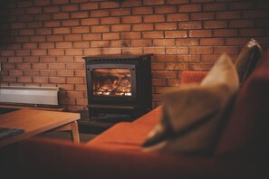A cozy room with a brick wall, a wood-burning stove, a sofa, and a table. - Aviemore Youth Hostel (Aviemore)