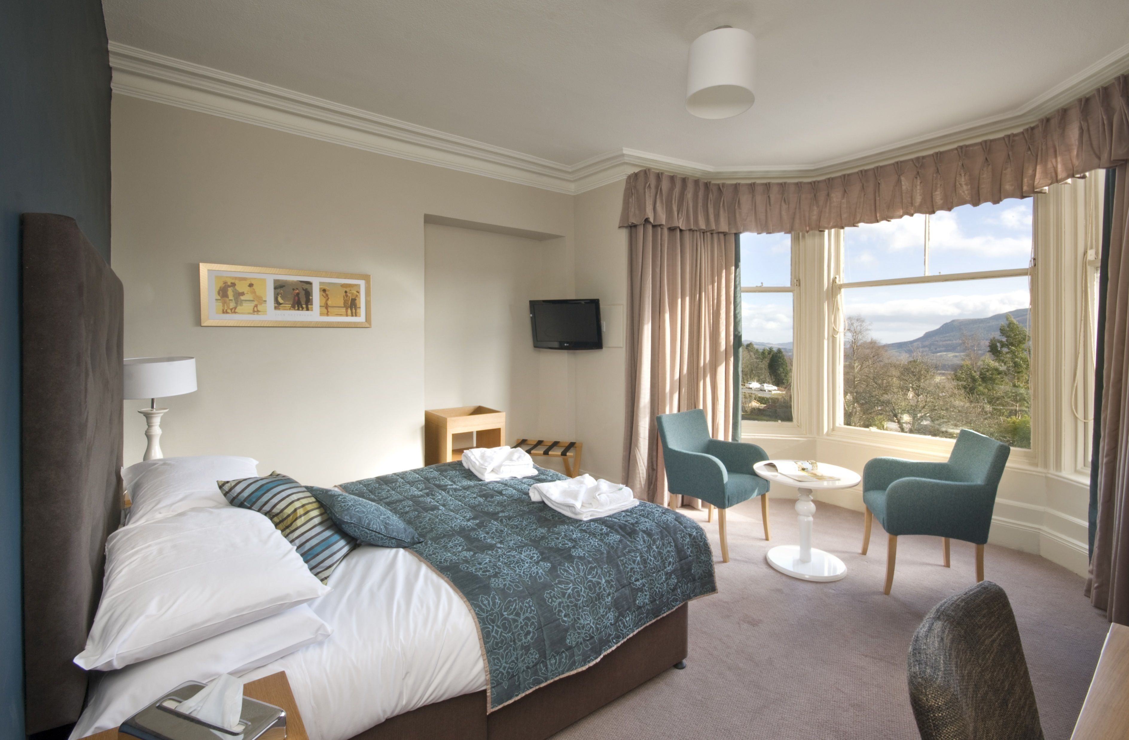 A hotel room with a bed, a TV, a desk, a chair, and a view of the outdoors.