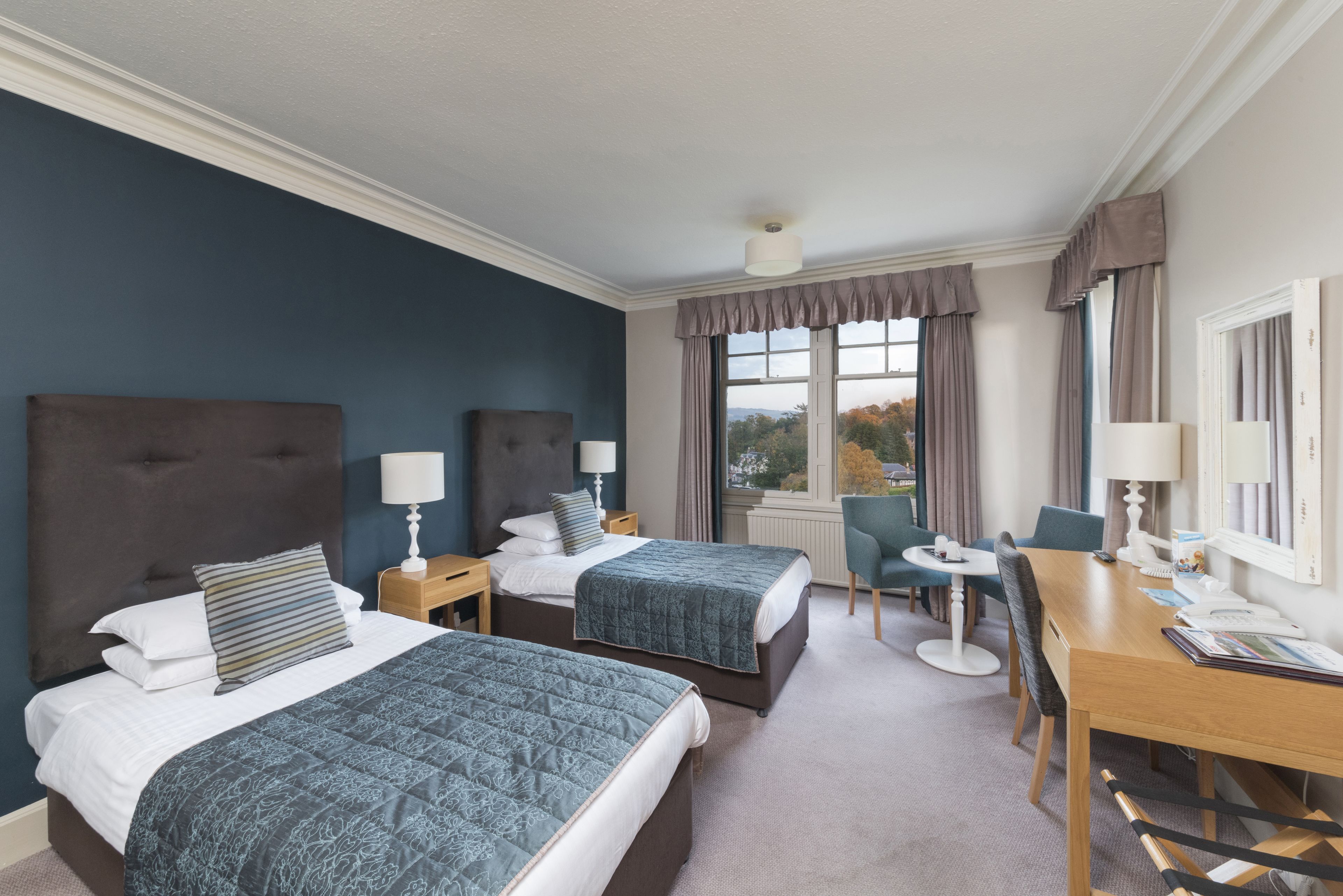 A hotel room with two beds, a desk, and a view of the outdoors.