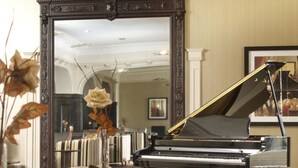 A grand piano in a spacious room with a large mirror and striped furniture. - The Pitlochry Hydro Hotel (Pitlochry)