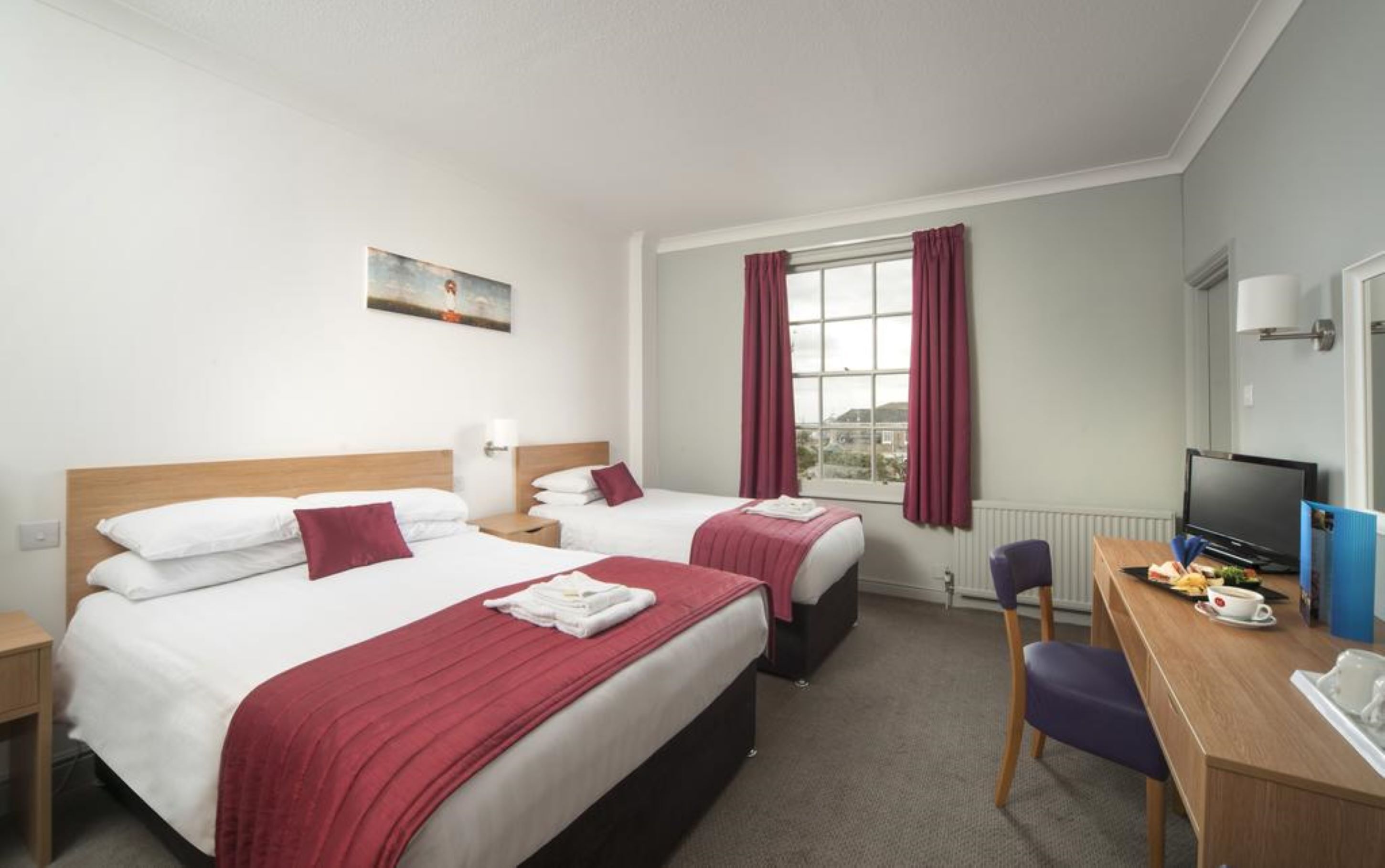 A hotel room with two beds, a desk with a computer, a chair, and a window with curtains.