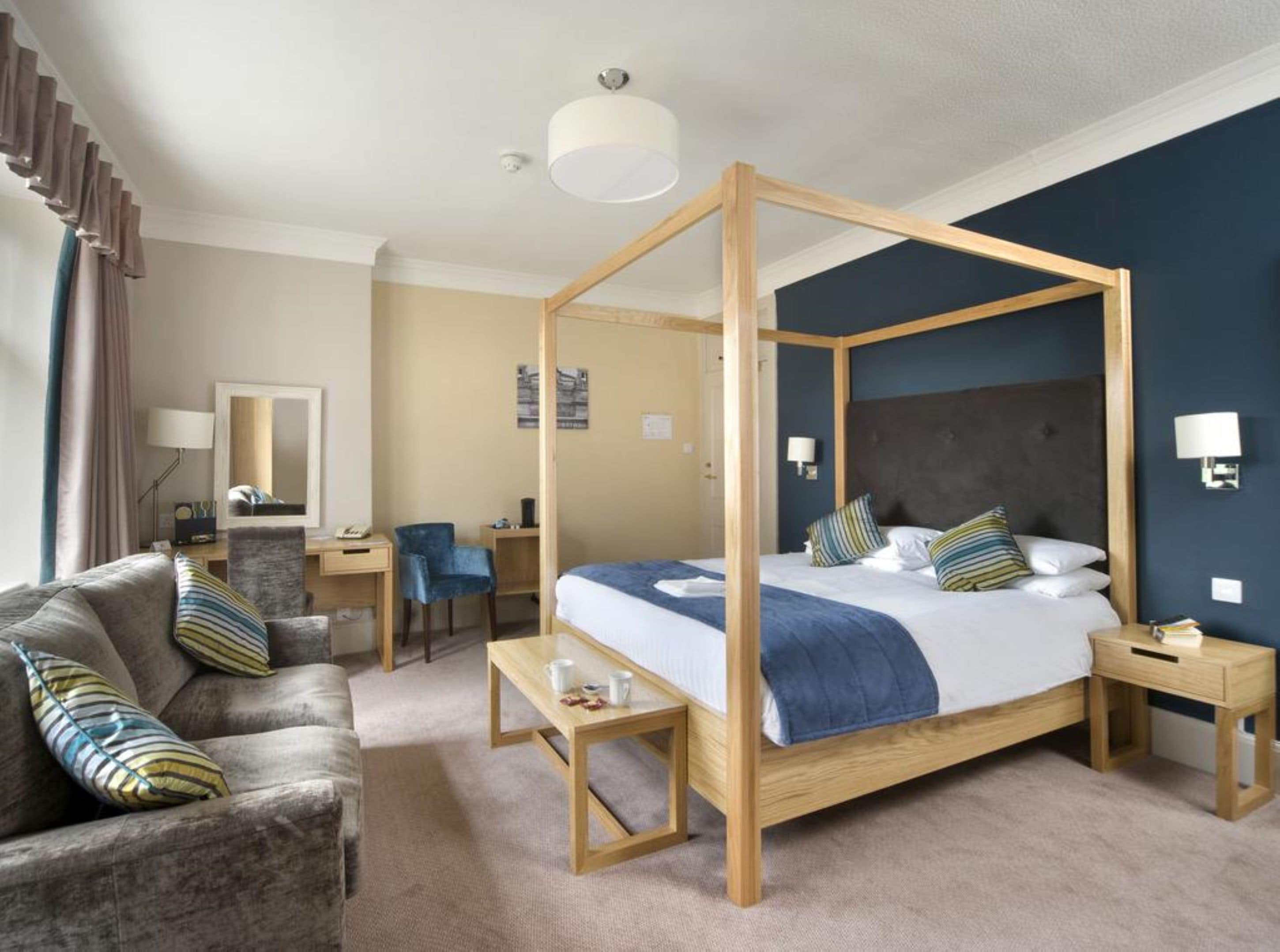 Een hemelbed met houten frame, een bureau met stoel, een bank en een nachtkastje met lamp.