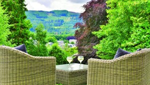 A wicker outdoor seating area with two chairs and a table, overlooking a lush green landscape with hills and trees. - The Pitlochry Hydro Hotel (Pitlochry)