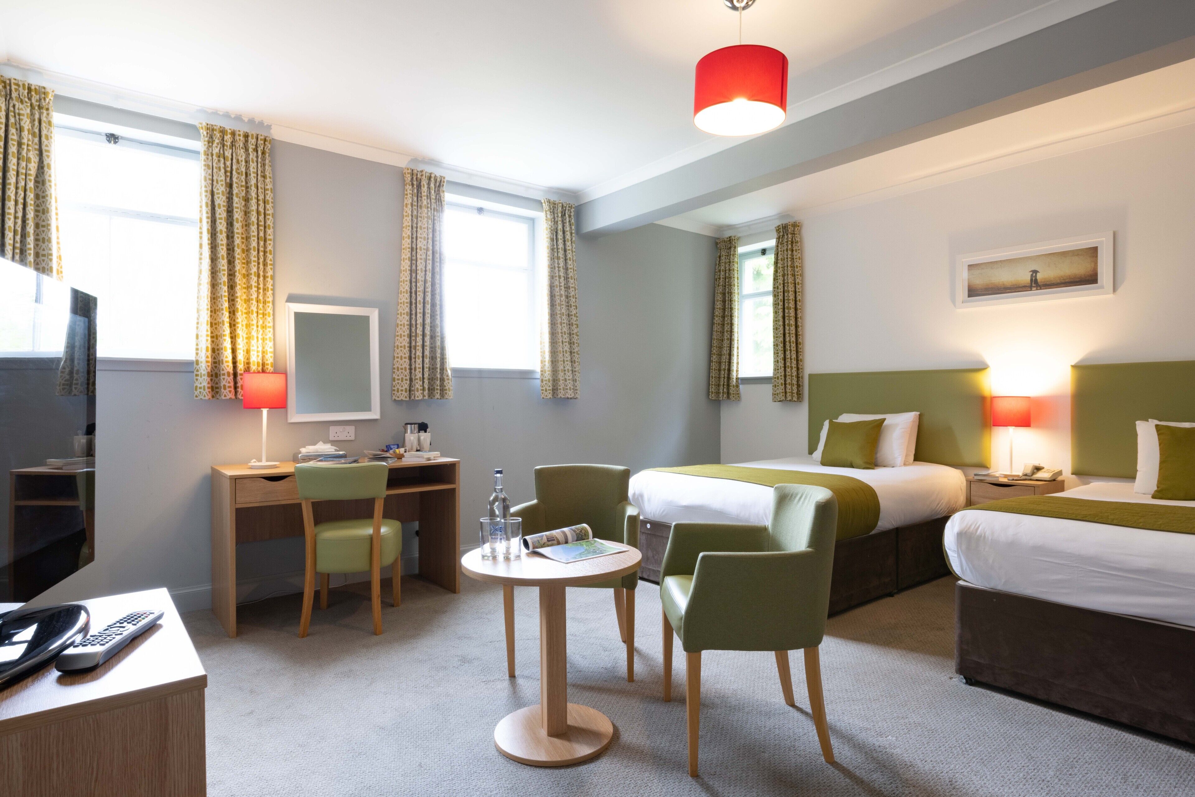 A hotel room with a bed, two chairs, a desk, a table, and a TV.