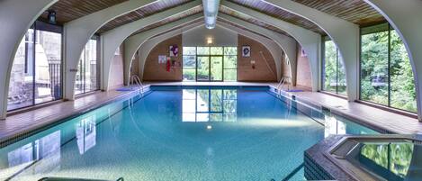 Una piscina interior con techo alto y ventanas arqueadas.