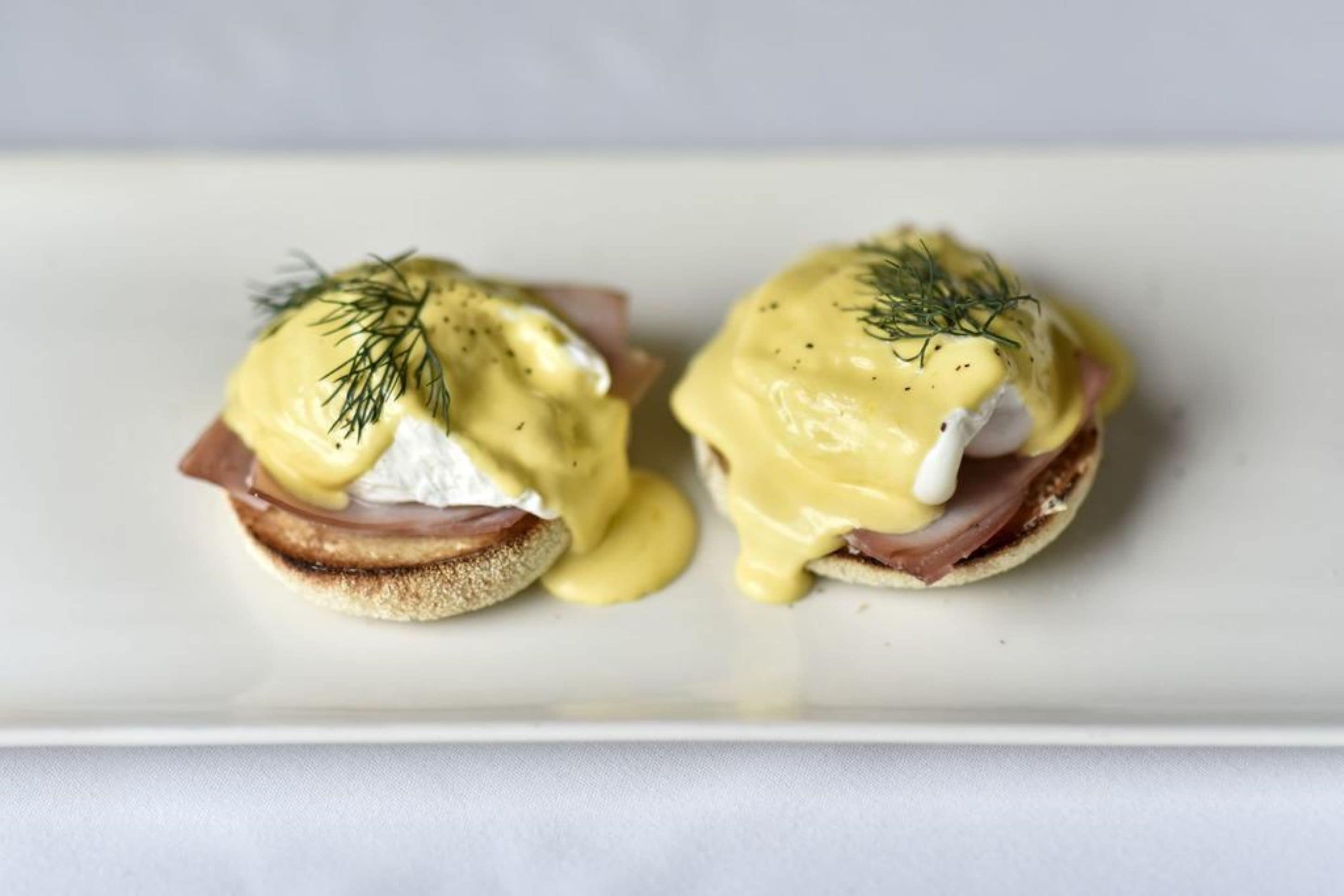 Two eggs benedict sandwiches on a white plate.