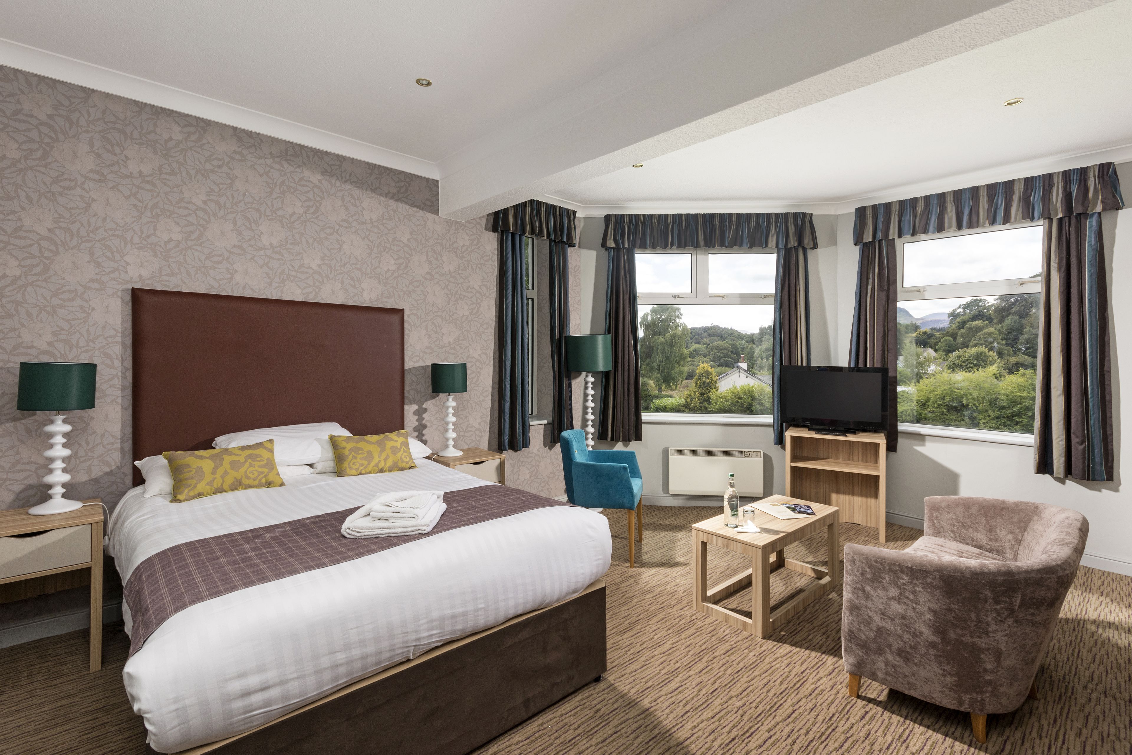 A hotel room with a large bed, a TV, a desk, and a chair.
