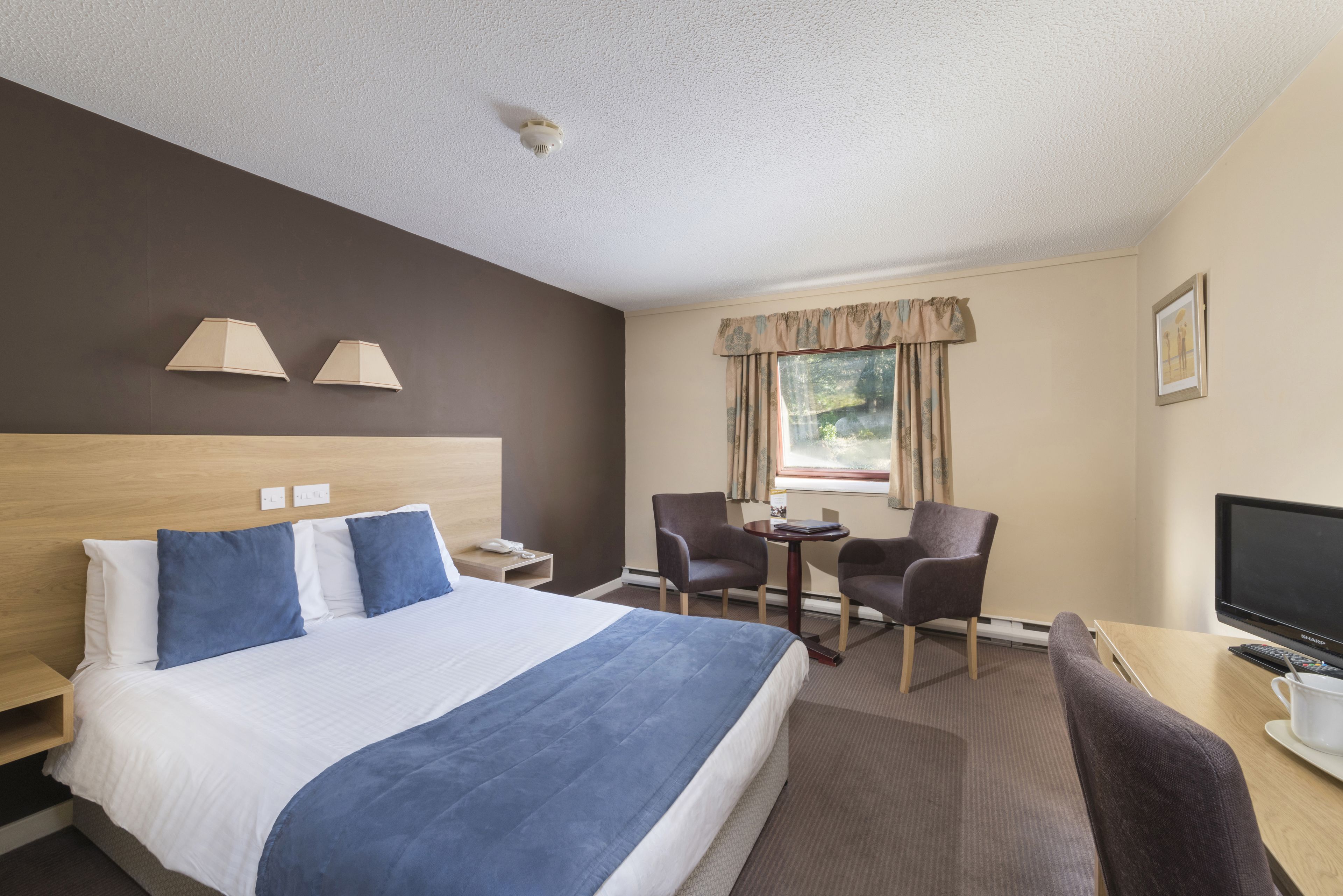 Ein Hotelzimmer mit einem großen Bett, zwei Sesseln, einem Schreibtisch mit Computer und einem Fernseher.