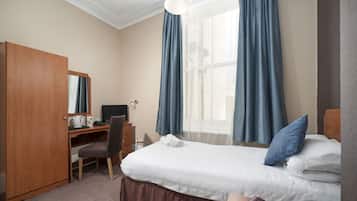Habitación de hotel con cama, escritorio con ordenador, silla, armario y ventana con cortinas.