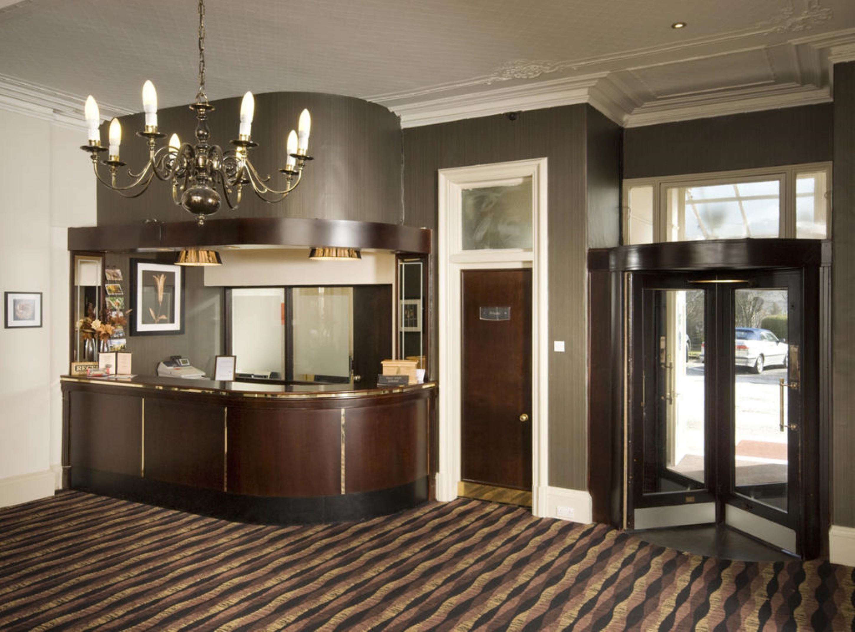 A reception area with a dark wood reception desk, a chandelier, and a patterned carpet.