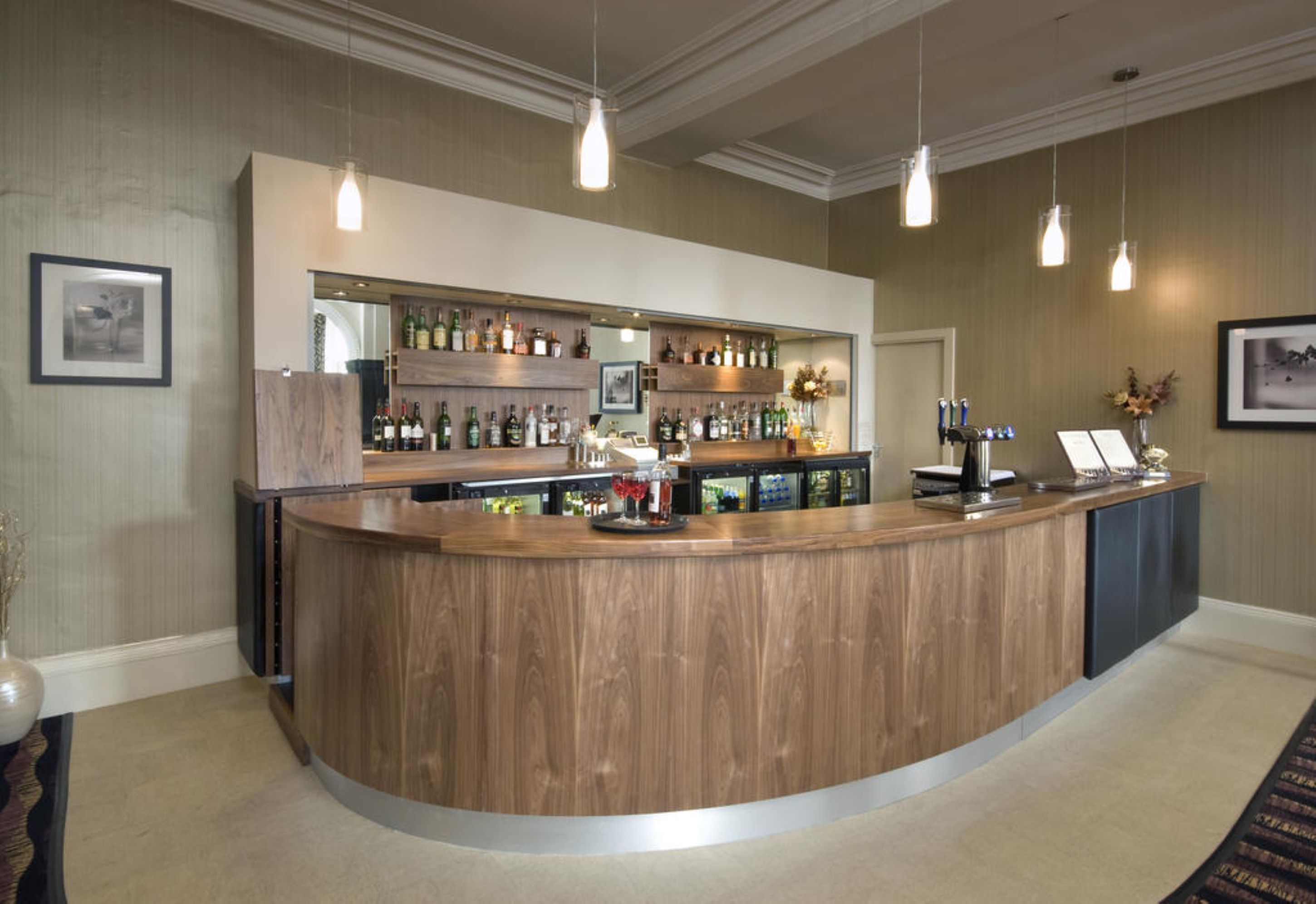 A curved wooden bar with shelves of bottles and a cash register.