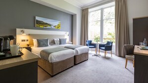 A hotel room with two beds, a desk, a chair, a coffee machine, and a window with curtains. - The Pitlochry Hydro Hotel (Pitlochry)