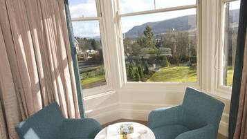 A room with two teal chairs, a white table, and a view of a landscape through large windows.