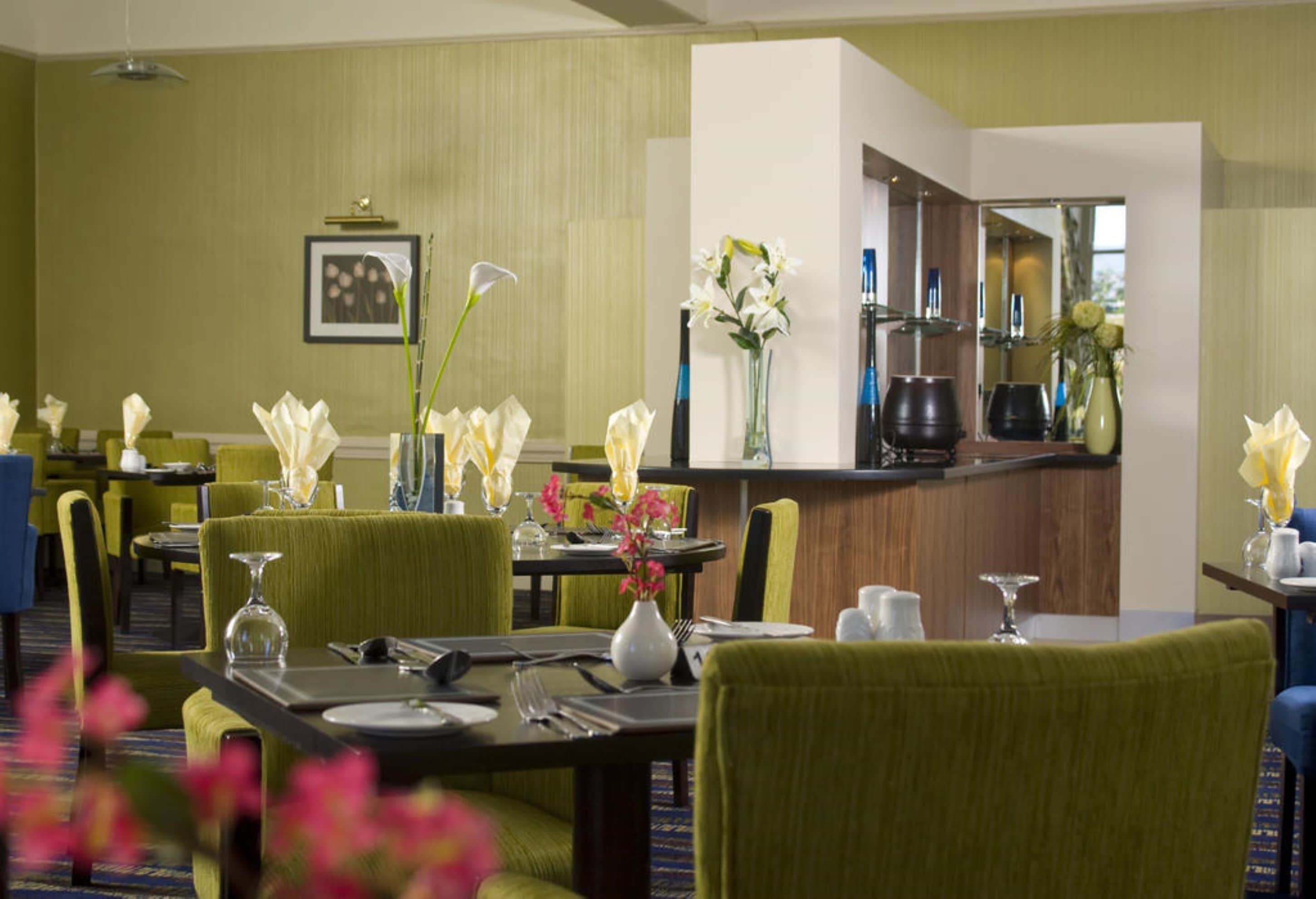 A hotel dining area with tables set for dining, chairs, and a bar area with a mirror and shelves.