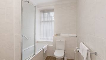 A bathroom with a glass shower enclosure, a toilet, a bathtub, and a window with curtains.