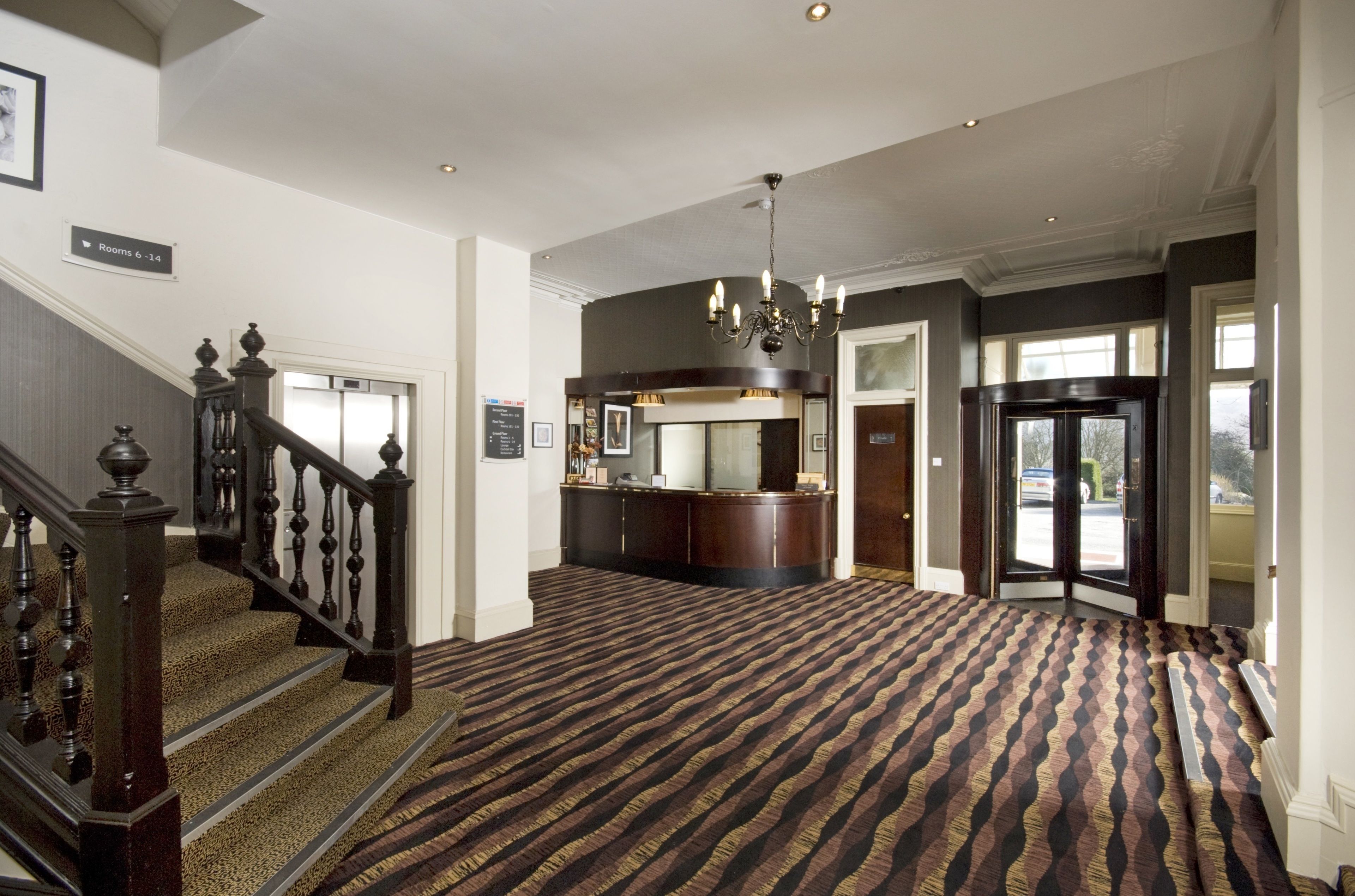 A hotel lobby with a grand staircase, a reception desk, and a patterned carpet.