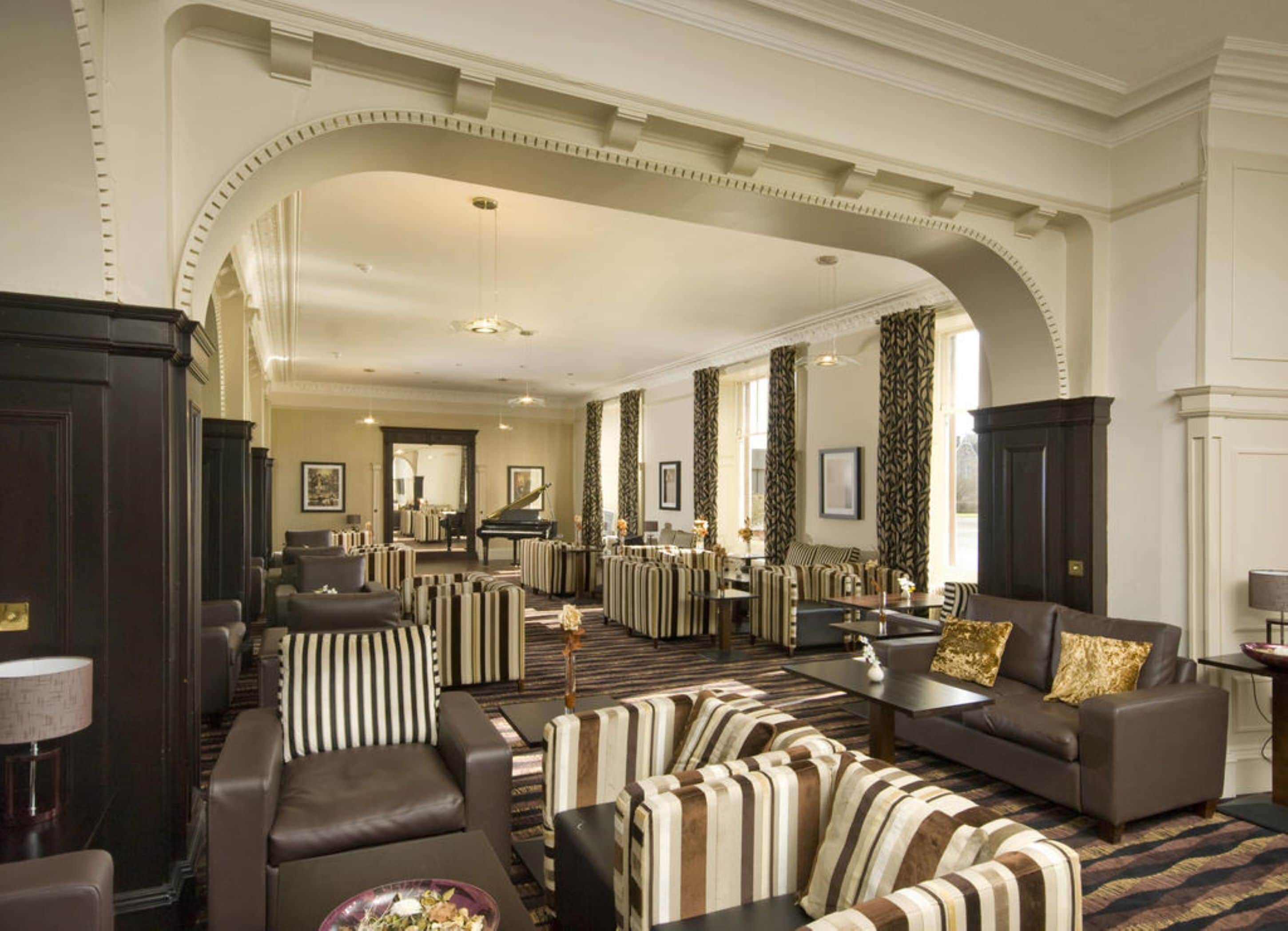 A spacious hotel lobby with a grand archway, multiple seating areas, and a piano.