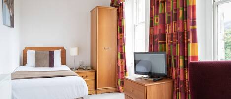 Habitación de hotel con cama, armario de madera, televisor sobre un aparador de madera y ventana con cortinas.