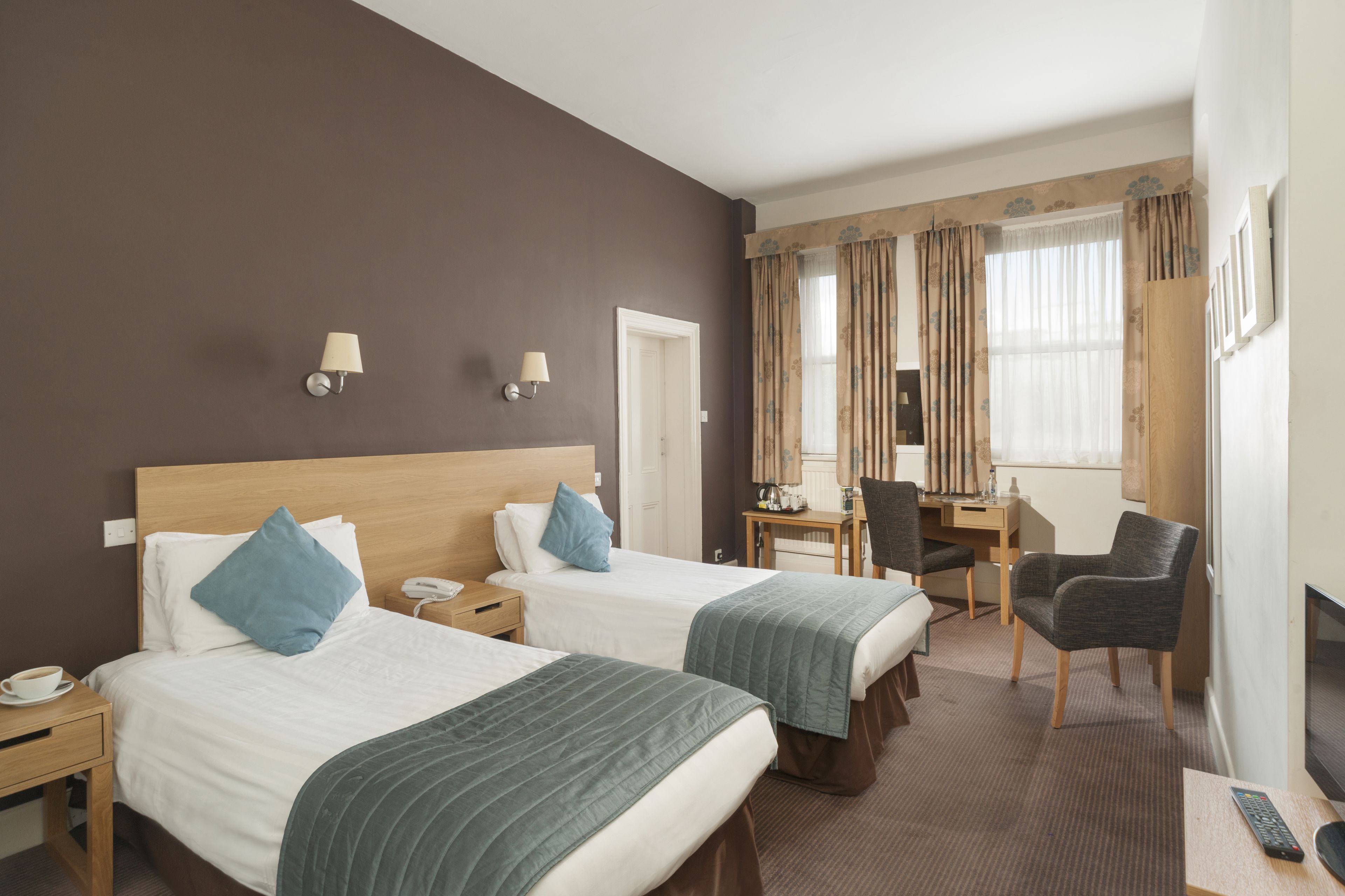 A hotel room with two beds, a desk, a chair, a TV, and a phone on the nightstand.