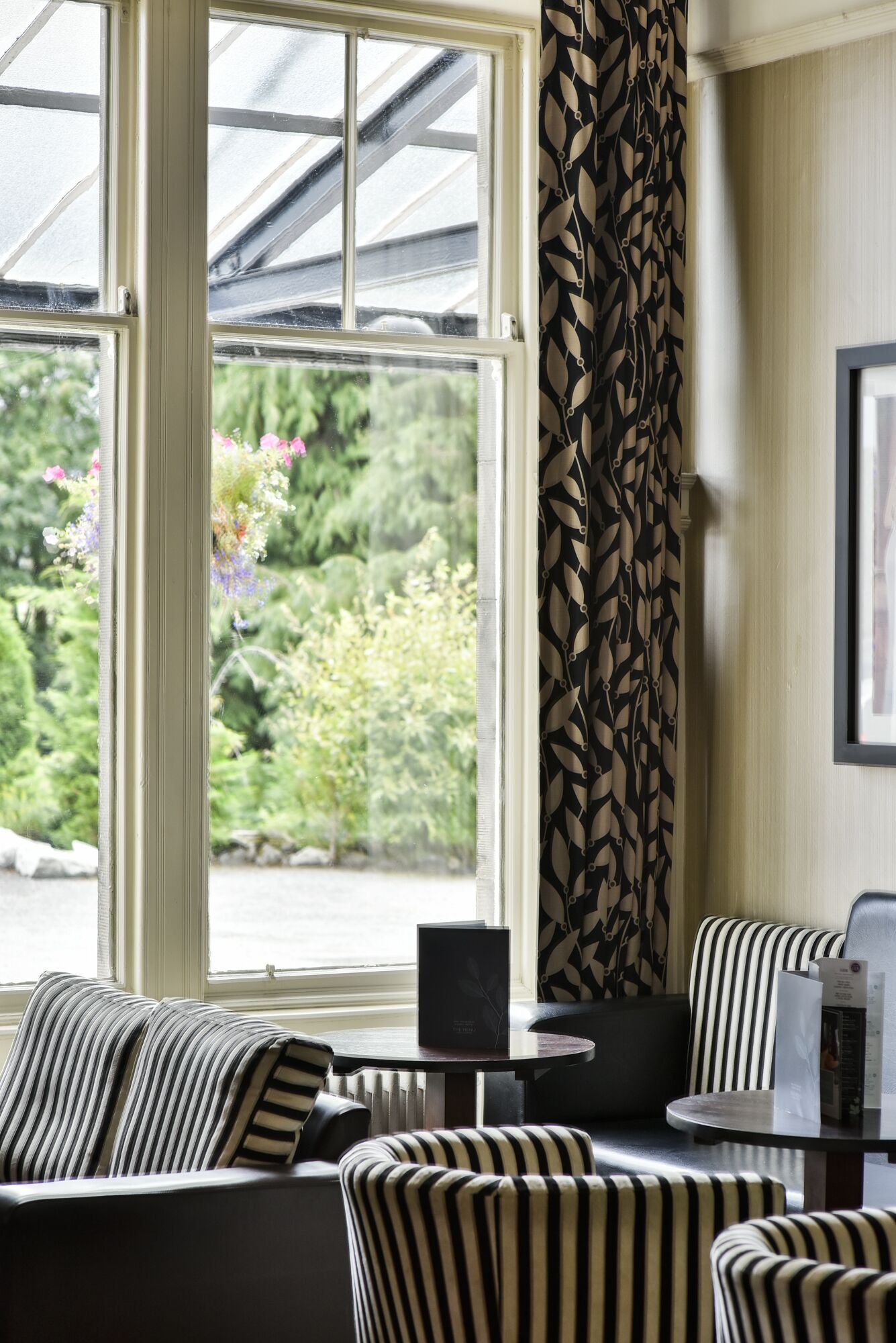 A room with a large window, striped chairs, a small table, and a patterned curtain.