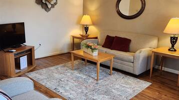 Een woonkamer met een bank, een salontafel, een televisie op een houten meubel en twee lampen op bijzettafeltjes.