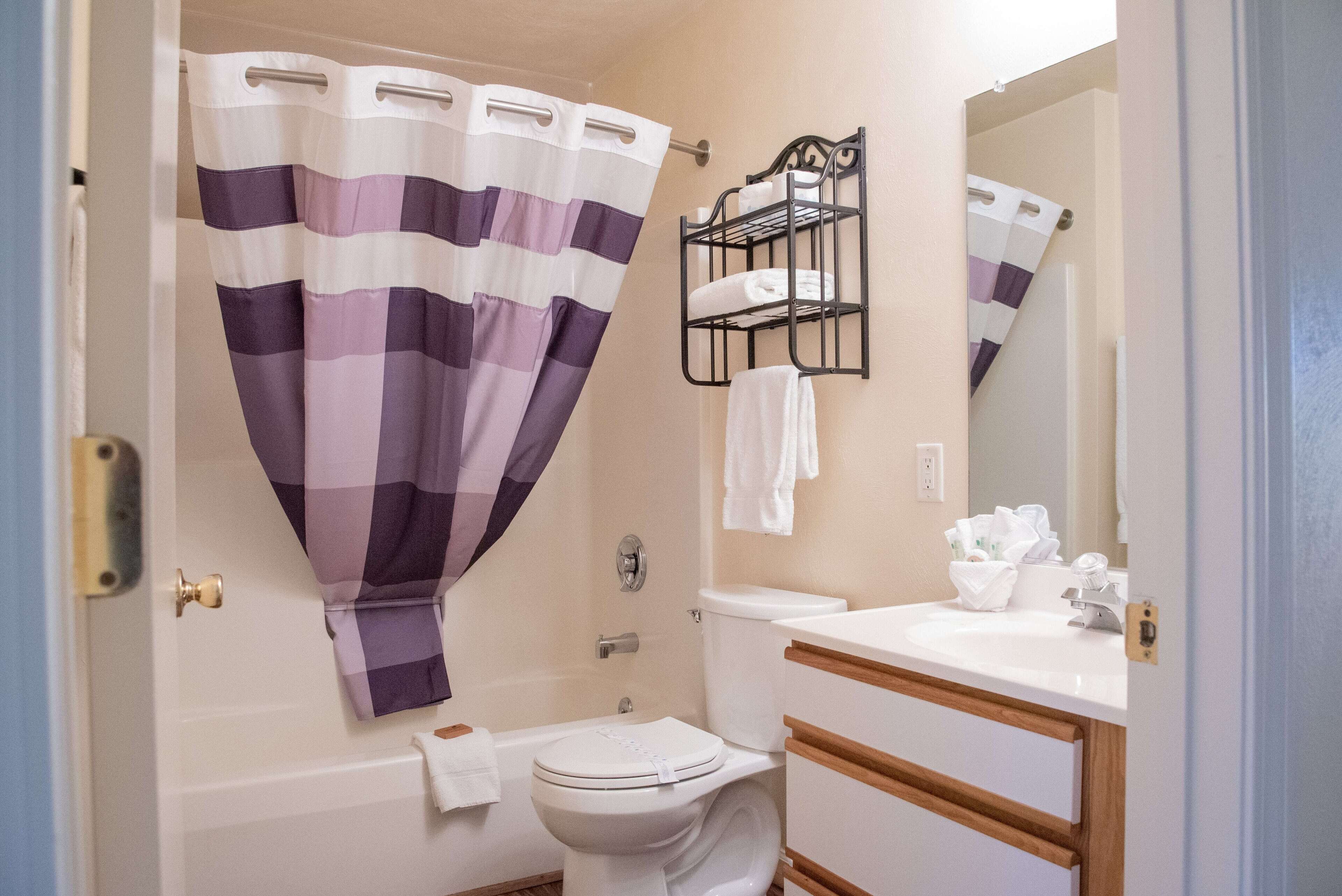 A bathroom with a shower curtain, a toilet, a bathtub, a sink, and a towel rack.