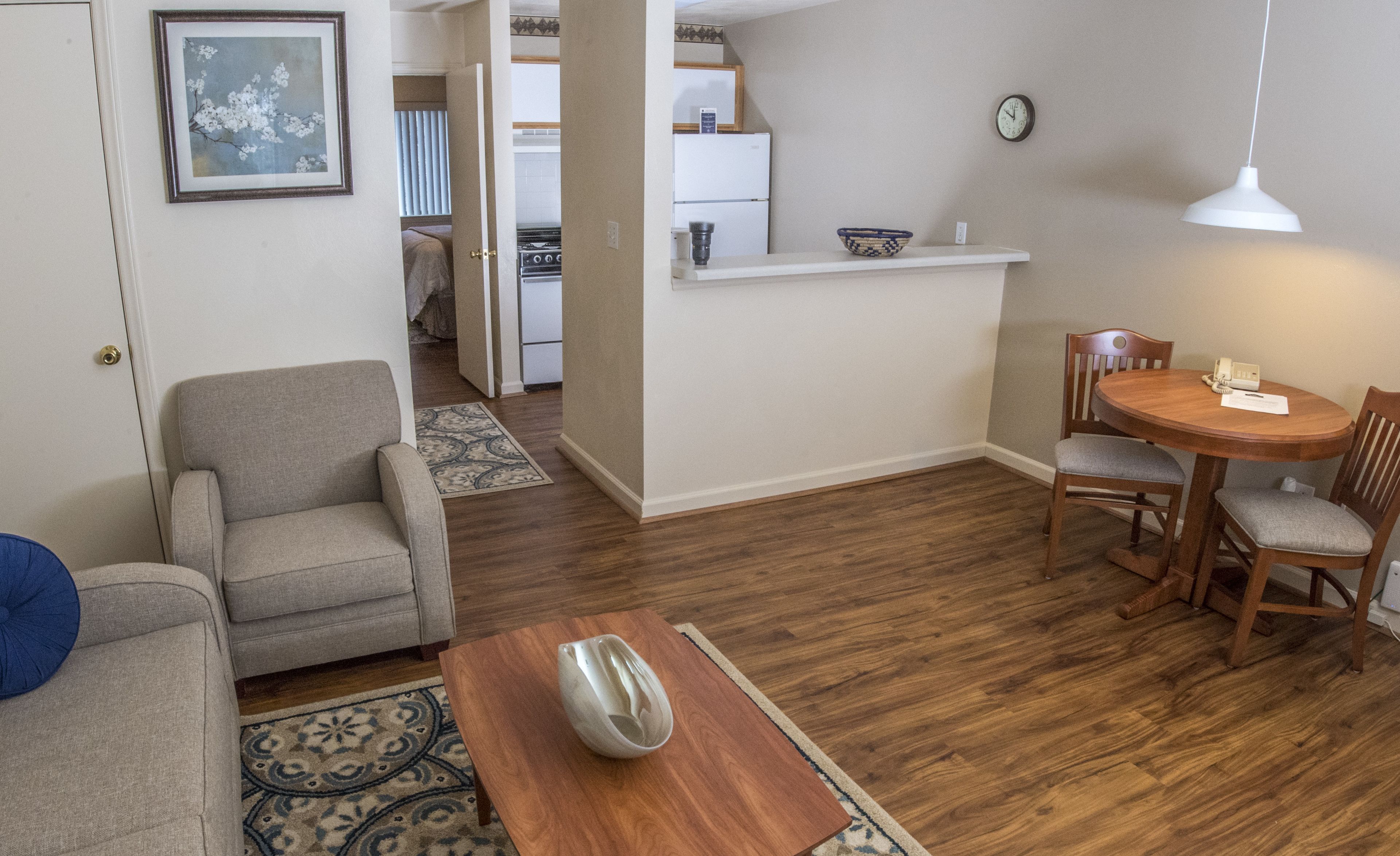 Sala de estar com sofá, mesa de centro e área de jantar com mesa e cadeiras. Cozinha visível ao fundo.