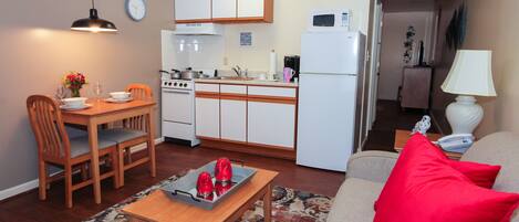 Een compacte leefruimte met een eethoek, kitchenette en een bank met rode kussens.