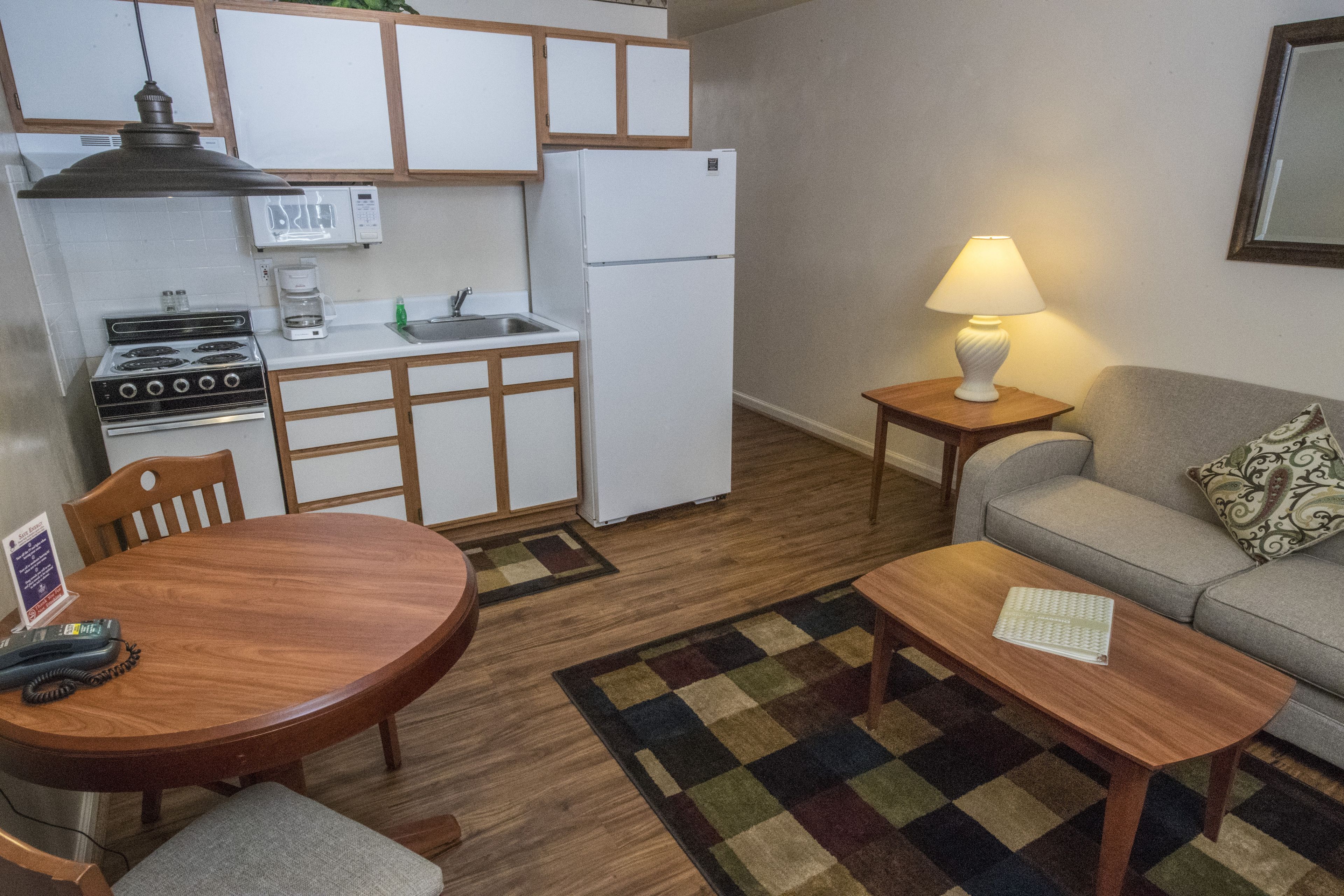 Eine kleine Küche mit Herd, Spüle und Kühlschrank, ein Esstisch mit Stühlen, ein kleiner Teppich und ein Sofa mit Lampe.