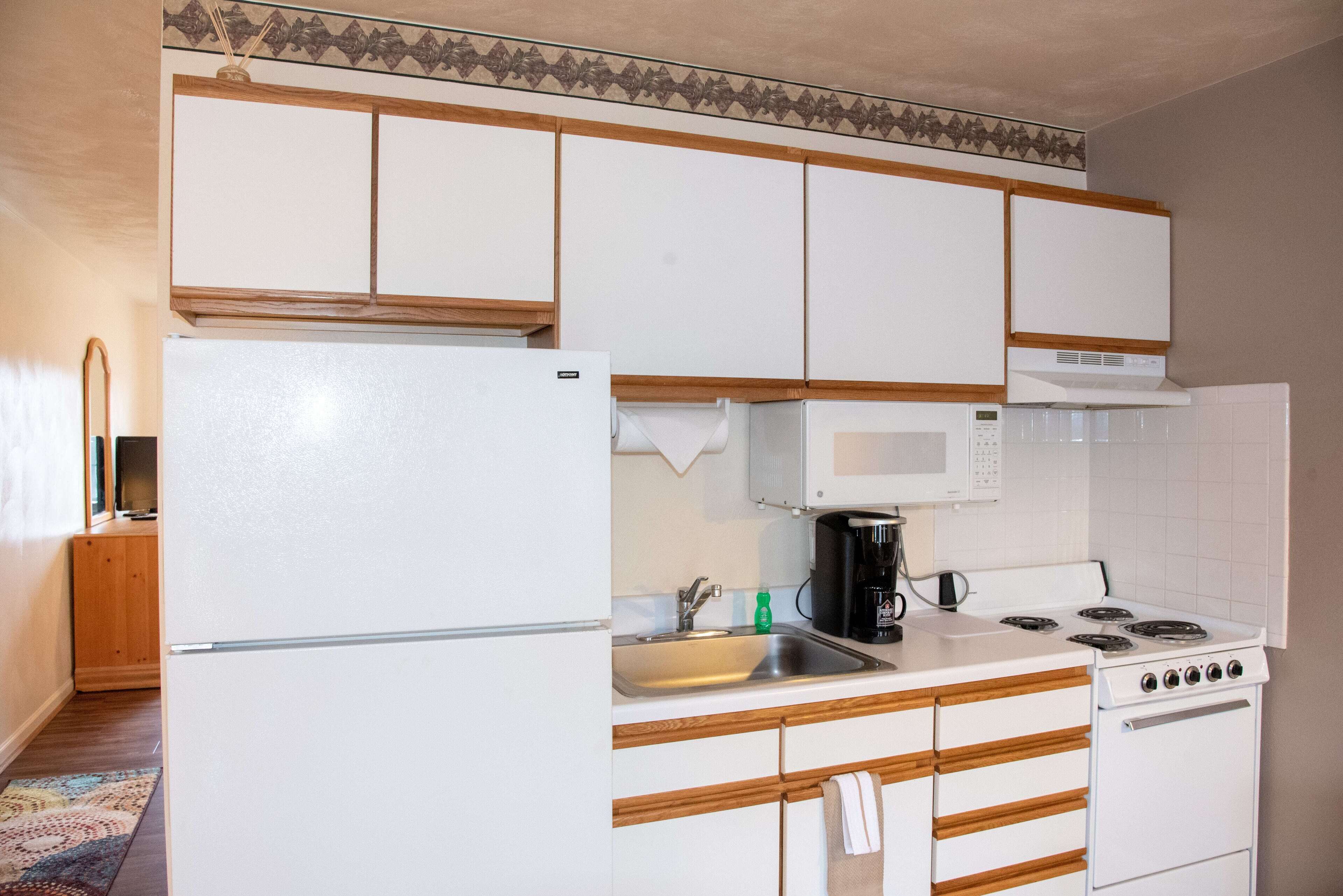 A compact kitchen with white cabinets, a refrigerator, a microwave, a stove, and a sink.