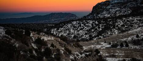 A mountainous landscape with snow-covered slopes and a sunset in the background.
