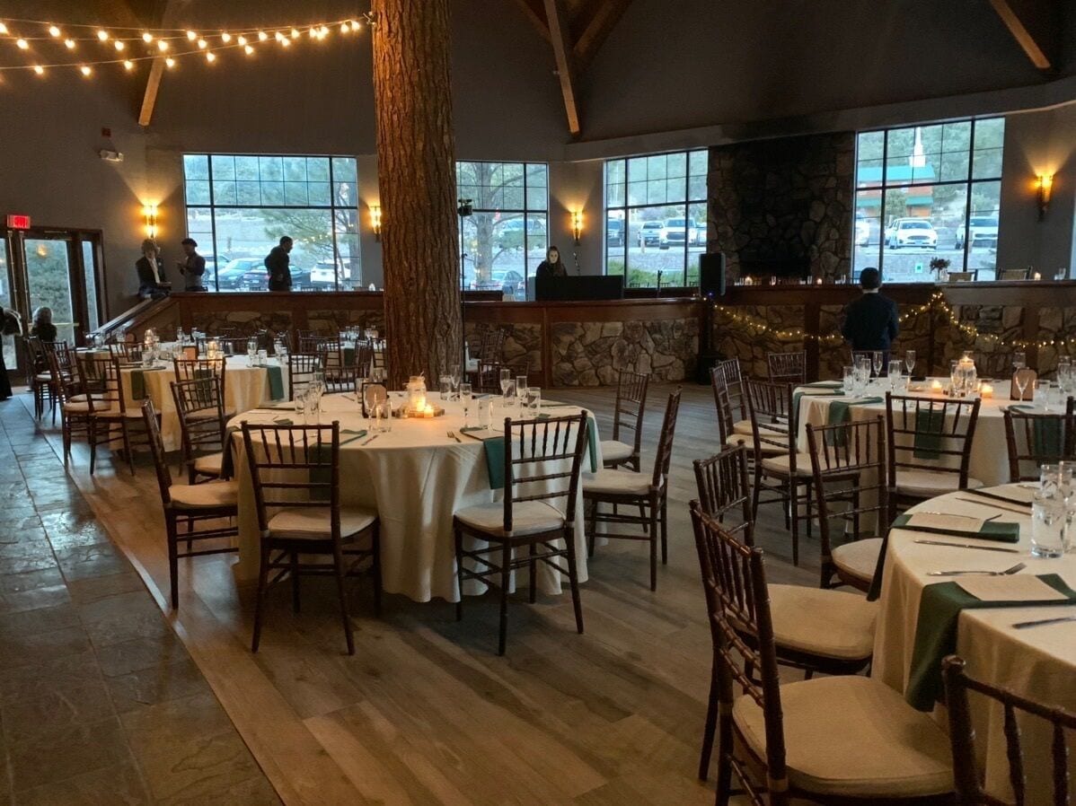 A restaurant with round tables set for dining, large windows, and a stone wall.