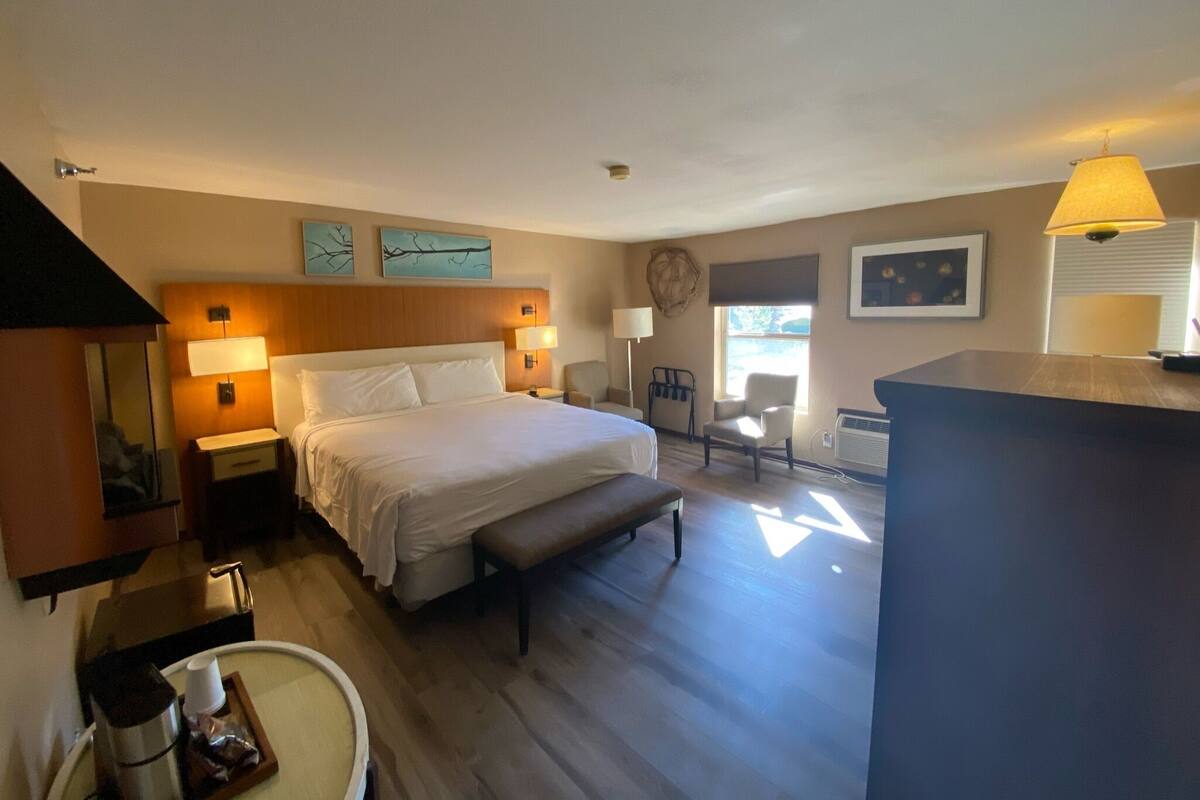 Una habitación de hotel con una cama grande, mesitas de noche, un escritorio y una silla. Hay una ventana que proporciona luz natural y vistas al exterior.