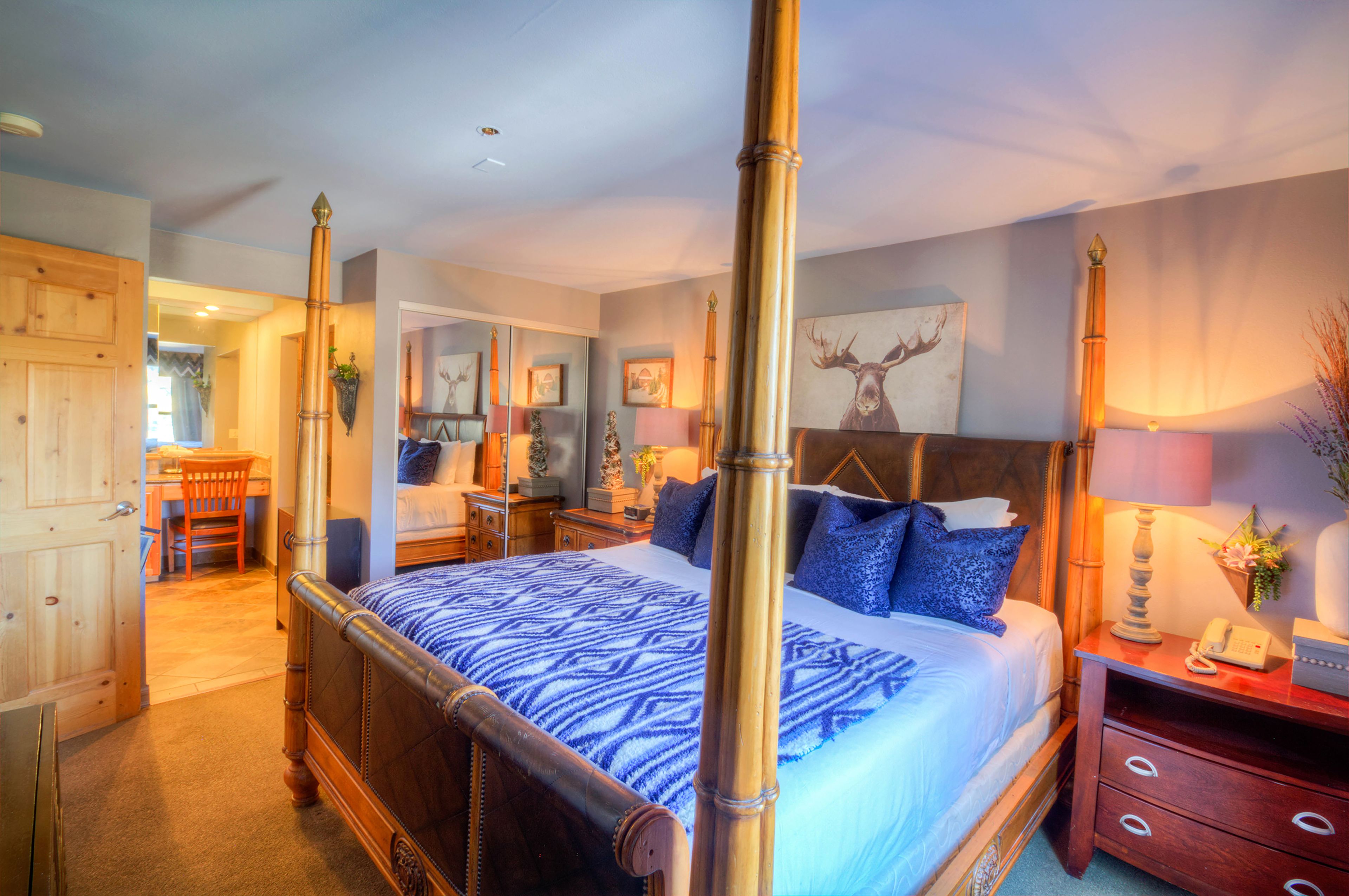 A four-poster bed with a patterned bedspread, a bedside table with a lamp, and a mirror above the bed.