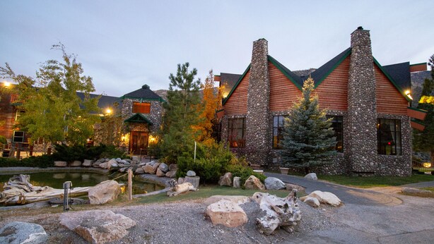 A lodge with a stone chimney, wooden exterior, and a pond in the foreground.