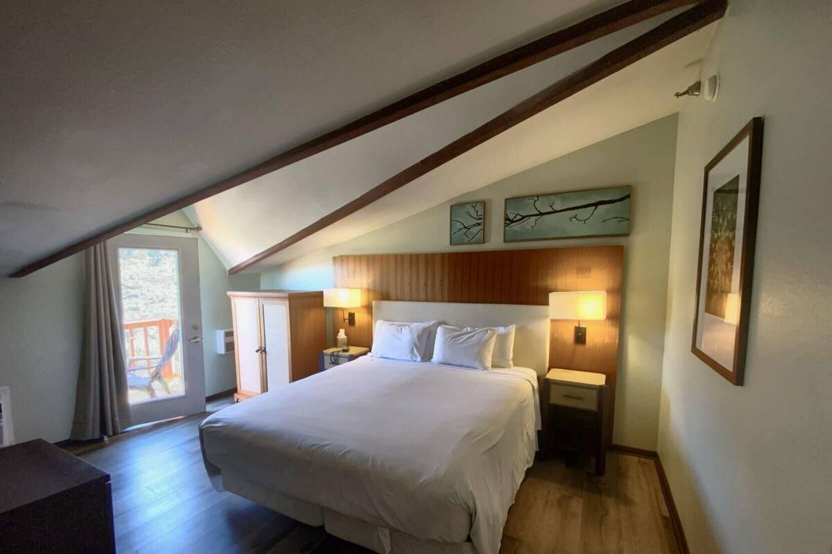 Un dormitorio con una cama grande, dos mesitas de noche con lámparas, un armario y vistas a través de una puerta.
