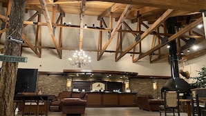 A spacious lobby with wooden beams, leather seating, a stone fireplace, and a sign indicating a restaurant.