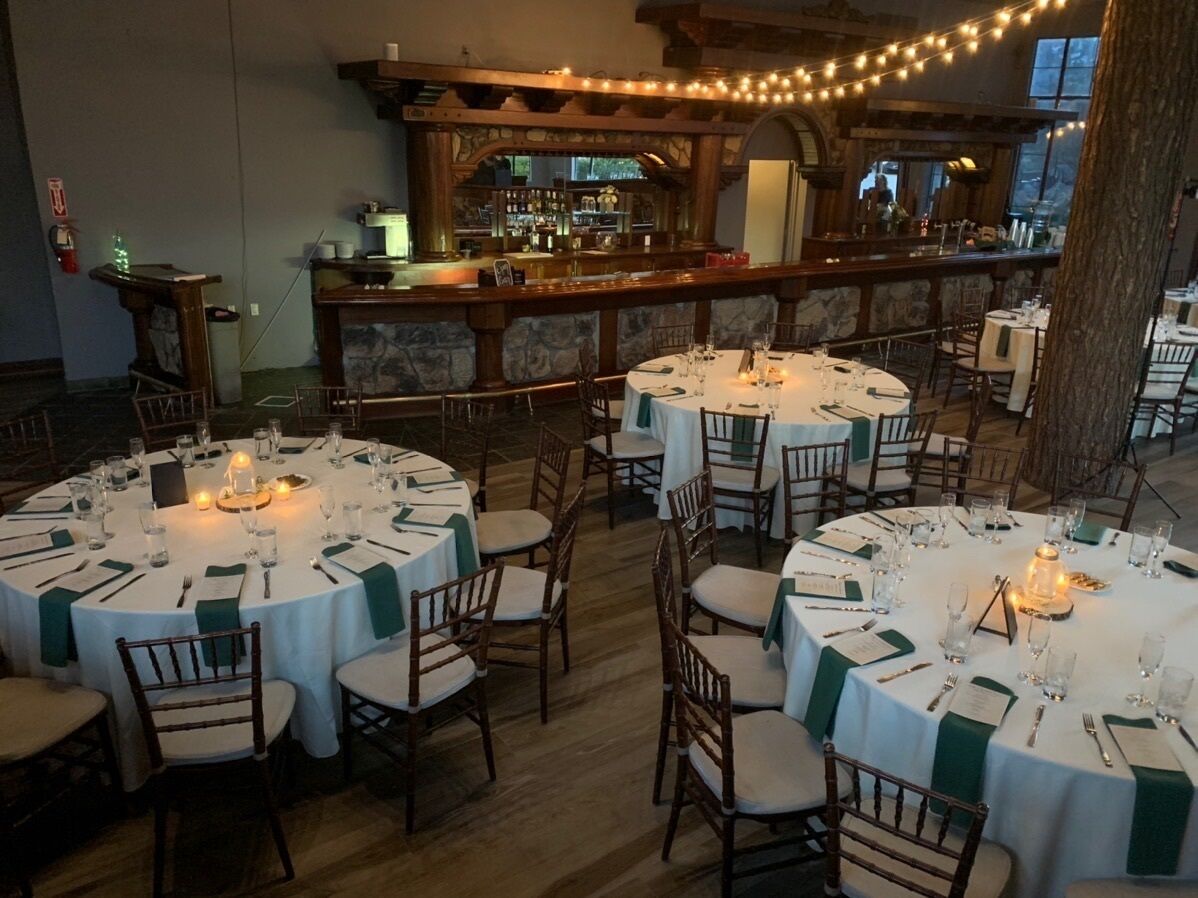 A restaurant with round tables set for dining, a bar area, and a view of the outdoors.