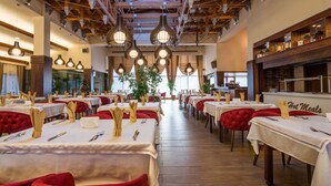 Restaurante com várias mesas preparadas para refeições, com cadeiras estofadas vermelhas e toalhas de mesa brancas.