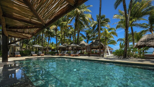 A clear pool with lounge chairs and umbrellas, surrounded by palm trees and a thatched-roof structure. - El Dorado Maroma, All & More Inclusive - Adults Only (Playa del Carmen)