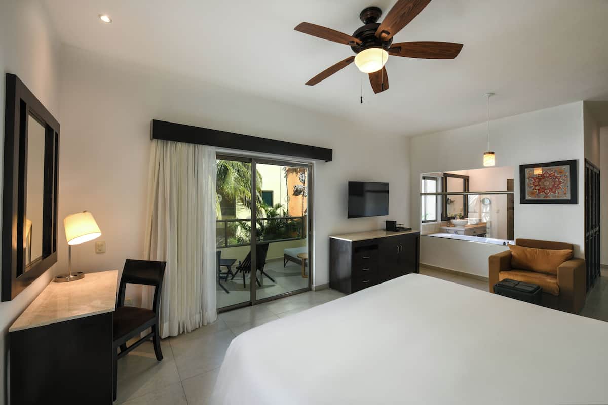 Een hotelkamer met een bed, bureau, stoel, televisie en een balkon met uitzicht.