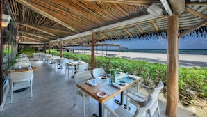 An outdoor dining area with thatched roof, wicker furniture, and a view of the beach. - El Dorado Maroma, All & More Inclusive - Adults Only (Playa del Carmen)