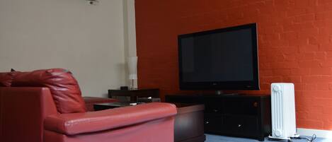 Sala de estar com parede de tijolos vermelhos, televisão de tela plana, sofá de couro vermelho e radiador branco.