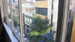 A view from a window overlooking a cityscape with modern and historic buildings, a tree, and a street. - YTI Garden Hotel (Melbourne)